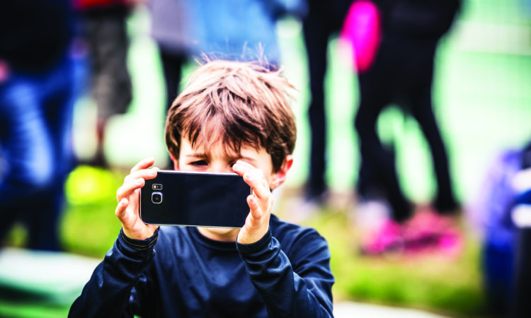 Young boy photographer taking photos using smartphone camera